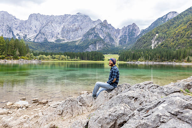 istock Man Sitting on Rock by Mountain Lake 2240930880