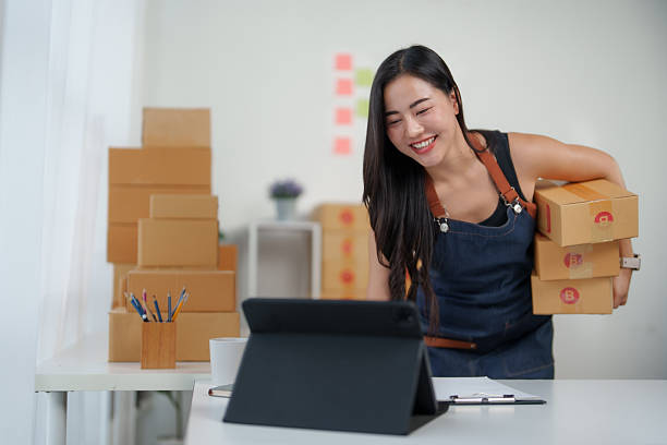 istock Asian female seller holding parcel boxes and looking at tablet screen 2240930958