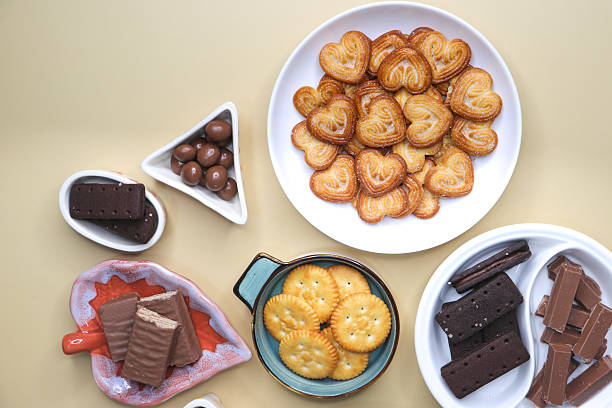 istock Assorted party snacks on table featuring chocolate cream sandwich biscuits, sugar coated heart cookies, wafer chocolates, chocolate coated caramel balls, salted crackers, and crispy potato chips. 2240931219