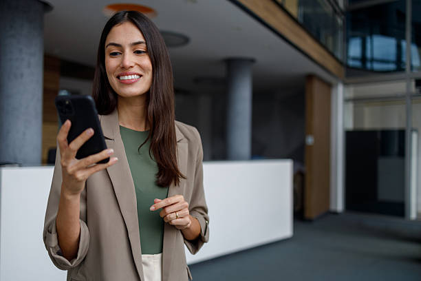 istock Businesswoman standing in modern office using mobile phone, checking messages, smiling for a successful day 2240931889