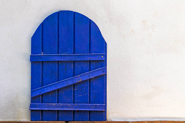 Arched rustic blue wooden gate with planks and a diagonal brace, set against a textured white plaster wall