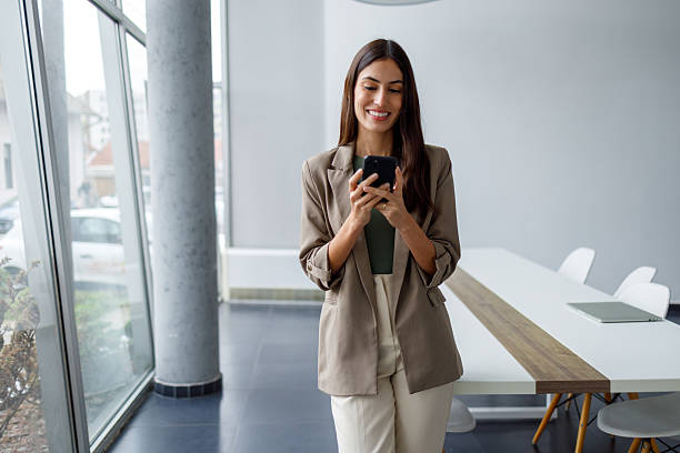 istock Businesswoman smiling, using smartphone inside modern office, connecting and networking for work and communication 2240932141