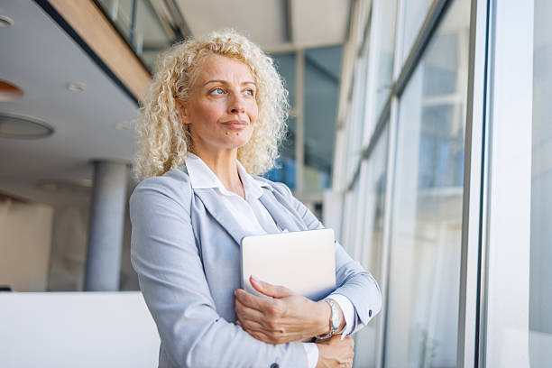 istock Businesswoman standing in office with digital tablet looking away 2240932196