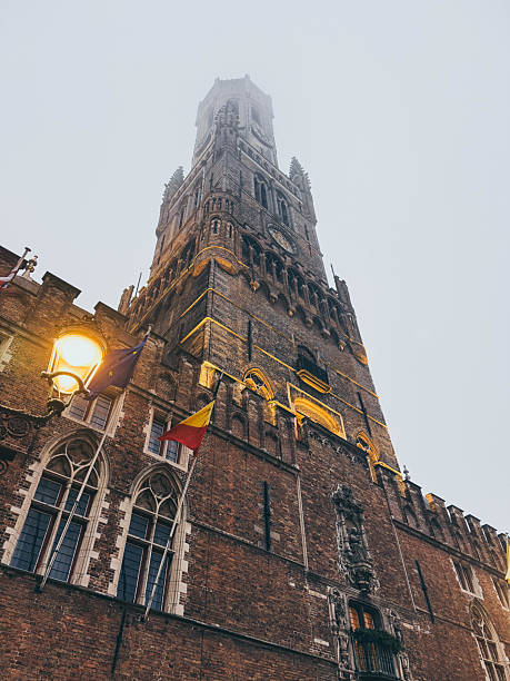 Low angle view. of  Belfry Tower of Bruges on a foggy day, historic Belgian landmark fading into misty winter atmosphere.