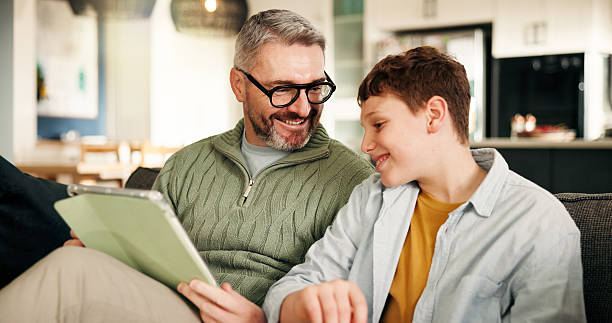 istock Home, father and son on sofa, tablet and bonding together with online game, relax and smile. Apartment, family and dad on couch, boy and parent with tech, social media and digital app with support 2240936687