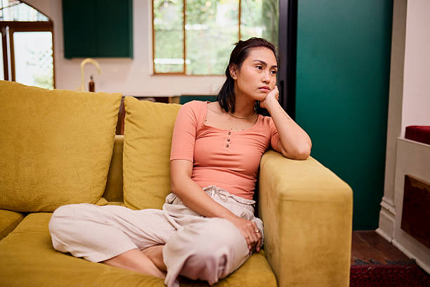 istock Contemplative Asian Woman Sitting on Couch Looking Away and Thinking 2240937013