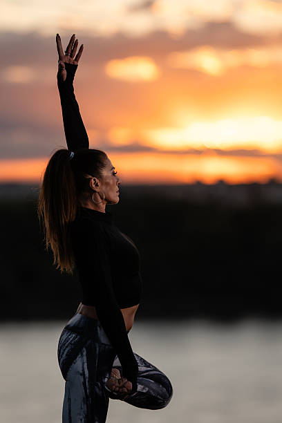 Yoga instructor practicing a balancing pose at sunset by the river, promoting wellness and mindfulness