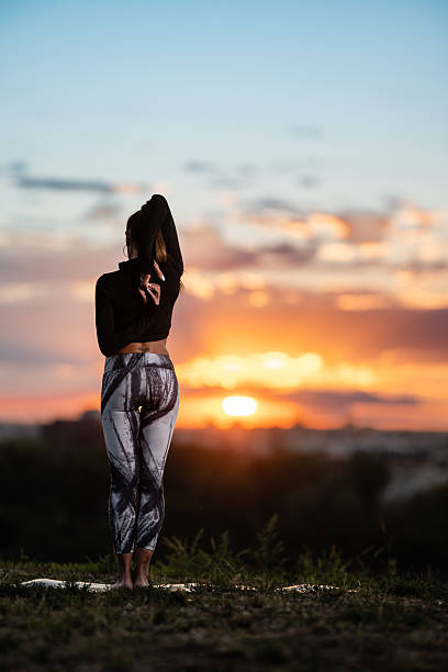 Yoga instructor performing a backbend stretch on a hilltop at sunset, embracing tranquility and mindfulness
