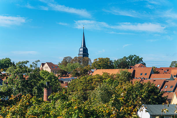 A picturesque Weimar skyline features a towering church steeple, red-tiled rooftops, and vibrant green trees under a bright blue sky. Ideal for travel, heritage, and architecture themes.