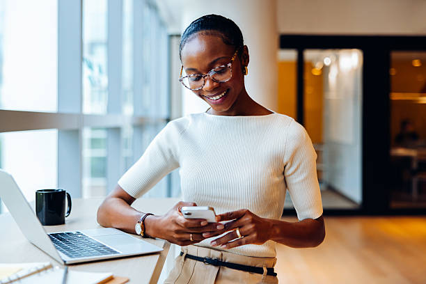 istock Professional woman using a smartphone at desk with a laptop 2240940909