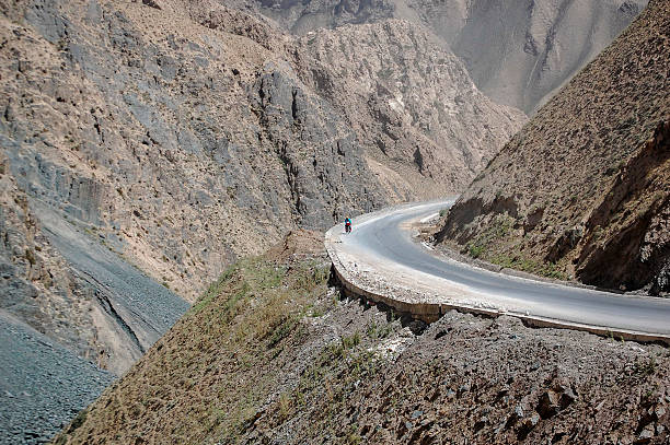 istock Winding road through mountainous terrain with a cyclist on it 2240942038