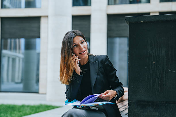 istock A businesswoman multitasks, engaged in a phone call while reviewing documents, exuding professionalism in a contemporary city backdrop. 2240947153