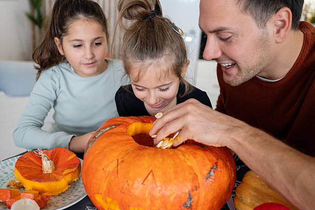 istock Father enjoying jack-o’-lantern carving for Halloween while daughters curious watching him 2240951687