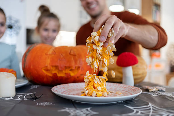 Dad girls scooping seeds from a jack-o’-lantern while daughters watching him