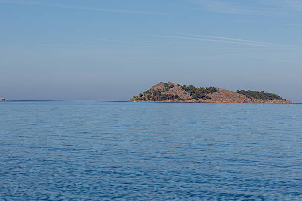 istock A serene island with sparse vegetation surrounded by calm blue sea under a clear sky. 2240951748