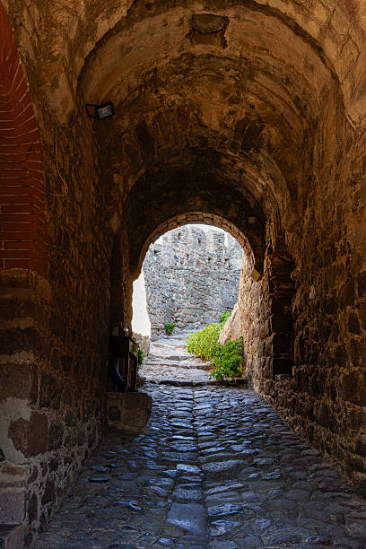 istock A stone archway leads to a sunlit path, surrounded by ancient stone walls. 2240952726