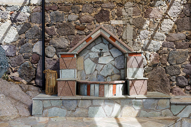 Stone fountain with geometric design against a rustic stone wall.