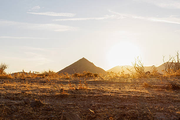 Sunset over a dry desert landscape with distant hills.