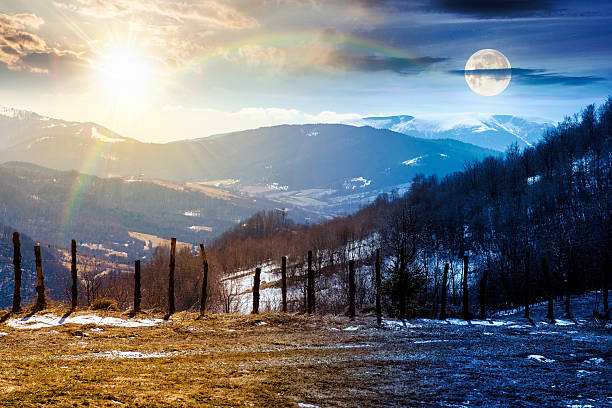 mountainous countryside on spring equinox. day and night time change concept. winter to spring season change scenery. melting snow and leafless trees on the rolling hills with sun and moon