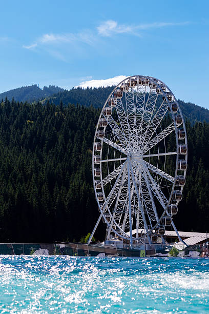 Ferris wheel against the backdrop of water and forested mountains.