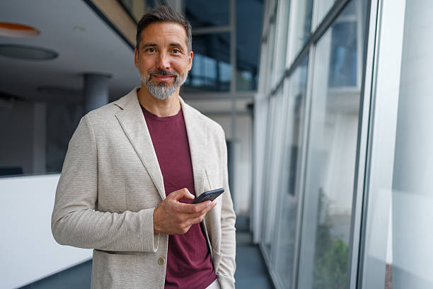 istock Confident mature businessman using phone in office, smiling at camera, communicating technology 2240958628