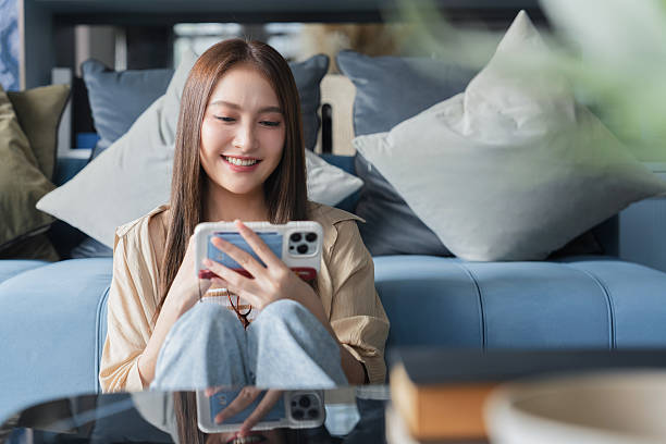 istock Young woman using mobile phone and smiling while sitting on floor at home 2240964080