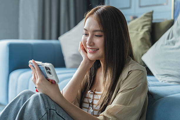 istock Young woman using mobile phone and smiling while sitting on floor at home 2240964085