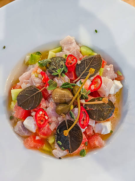 A colorful tuna ceviche with cucumber, watermelon, feta, chili, and caper leaves served in light citrus dressing at a seaside restaurant in Naxos, Greece.