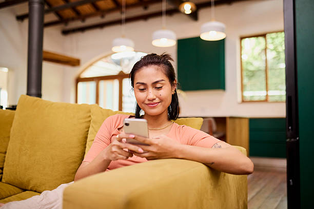 istock Happy Asian Woman Smiling While Relaxing and Using Mobile Phone on Couch 2240968256