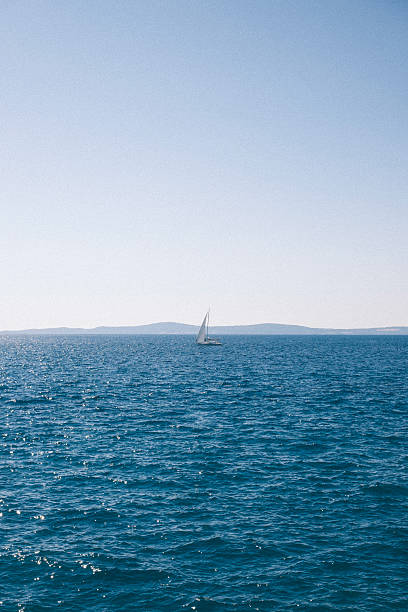 Small sailboat on a vast blue ocean with distant hills under a clear sky. High quality photo