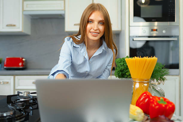 istock Young blonde woman with long hair using laptop in a kitchen 2240971648