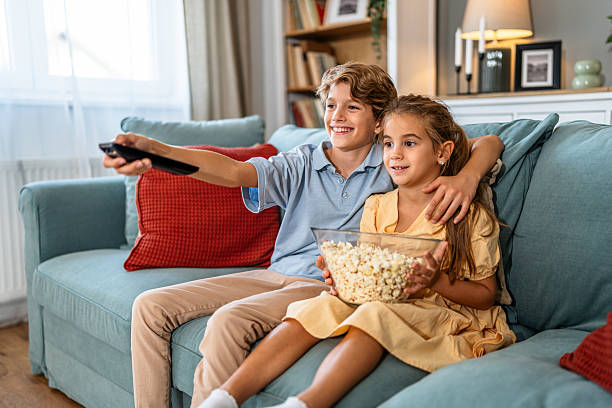 istock Siblings watching tv together eating popcorn at home 2240975497