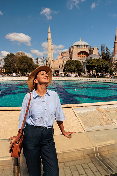 Woman enjoying a sunny day at Sultanahmet Square in Istanbul, Turkey, with the fountain and Hagia Sophia Mosque visible in the background, soaking in the vibrant atmosphere.