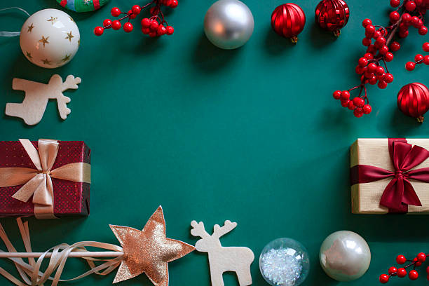 istock Christmas frame with baubles, wrapped gift boxes, berries, ribbon bows, golden glittery star, felt reindeer on dark green background with copy space 2240980013