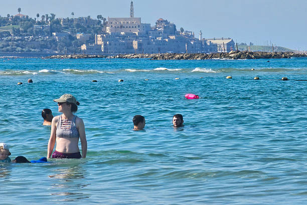 Tel Aviv, Israel - September 24, 2025: People swim in the water on a Mediterranean beach with the old city of Jaffa in the background