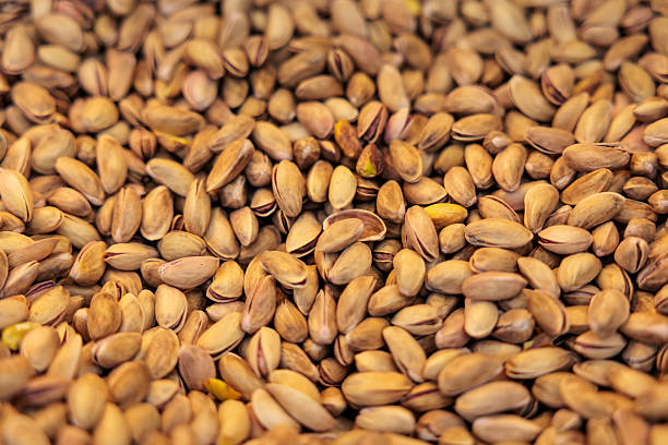High-resolution close-up image of roasted pistachios in their shells, showing natural texture and warm brown tones.