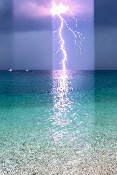 A powerful bolt of lightning pierces the sky, striking the ocean beneath a dark storm cloud. Captured with a mobile phone, the image contrasts the serene clarity of turquoise water in the foreground with the dramatic energy of the storm. A lone boat drifts to the left, adding scale and solitude to the scene. Vertical light bands from the lens create a surreal, layered effect, enhancing the tension between calm and chaos. Ideal for themes of nature’s power, solitude, or dramatic weather. Lens flare.