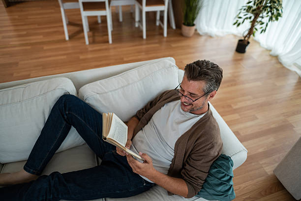 istock Man wearing eyeglasses reading book on couch at home 2240987685