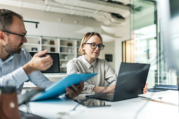 istock Professional office scene with colleagues collaborating and reviewing documents on laptops 2240988581