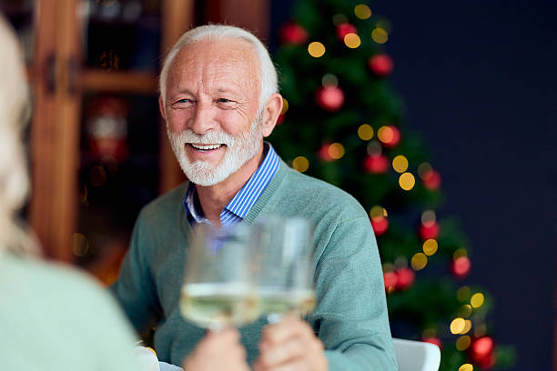 istock Smiling Elderly Man Toasting With Glasses During Christmas Celebration At Home With A Tree In Back 2240994239