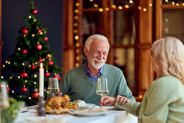 istock Warm Christmas Dinner With Elderly Couple Sharing Laughs By Christmas Tree And Candles 2240994247