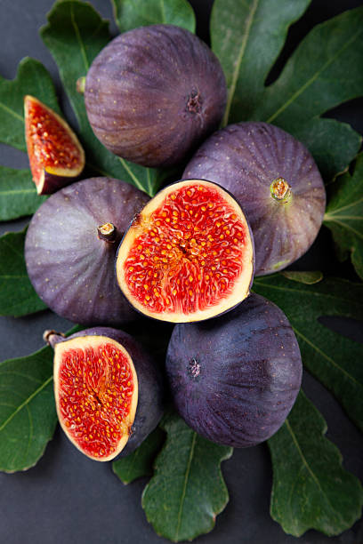 Fresh ripe figs with leaves on black stone background.