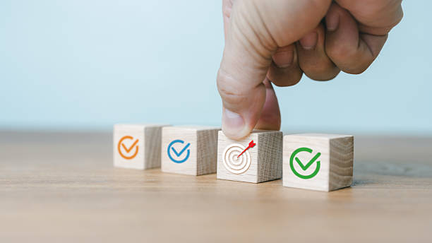 istock Hand placing wooden blocks with check marks and target icons representing goal achievement, business success, planning strategy, and progress management in professional organization. 2240999315