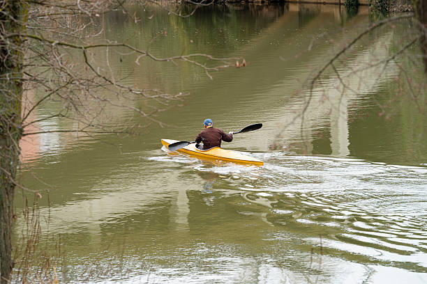 Middle-aged man paddling a yellow kayak alone on calm river, enjoying peaceful spring or autumn outdoor recreation and adventure, reflection and solitude in nature