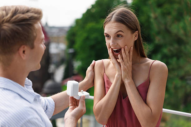 istock Man with engagement ring making marriage proposal to his surprised girlfriend on balcony outdoors 2241001390