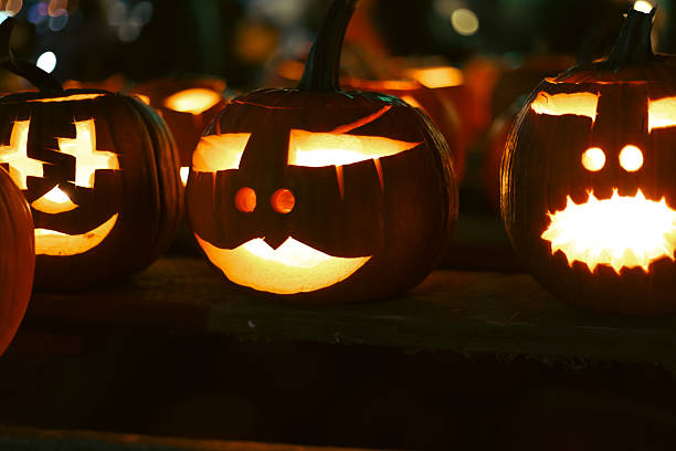 istock Carved glowing Halloween pumpkins with candles in dark night. 2241005100