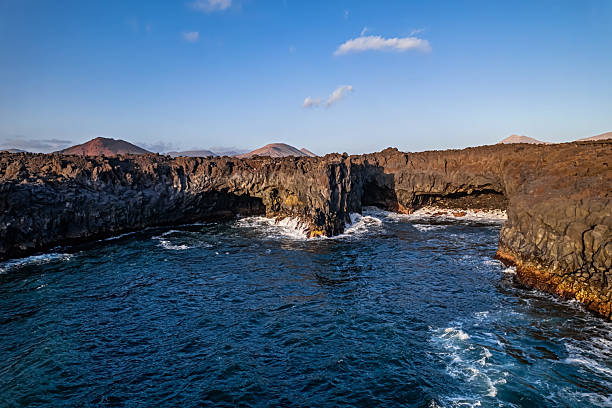 Scenic view of rugged volcanic cliffs and ocean waves crashing into sea caves at Los Hervideros viewpoint in Lanzarote, Canary Islands, Spain.
