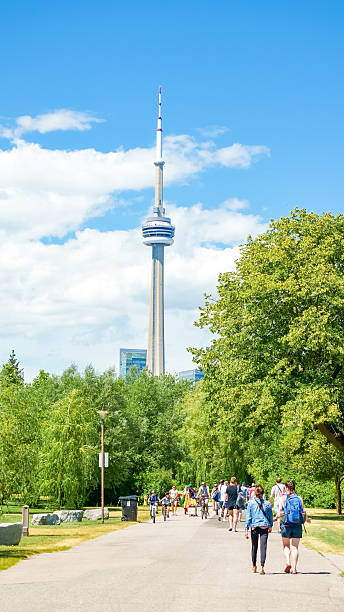 Toronto ON, Canada - July 03, 2022: CN Tower stands tall in Toronto, surrounded by greenery and people enjoying a sunny day in the park, creating a lively urban atmosphere