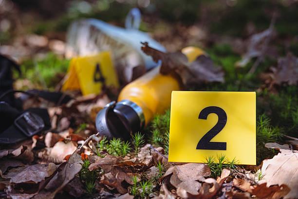 Middle-Aged Male Forensic Investigator Wearing White Protective Suit, Safety Glasses, Face Mask, Shoe Covers, And Blue Gloves At Crime Scene Investigation, Surrounded By Forensic Evidence Markers And Tools, With Background Of Abandoned Building Walls In Poor Condition.
