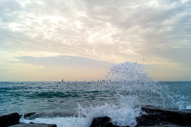 Energetic ocean scene of Lanzarote with crashing waves in the foreground and sailing boats scattered on the horizon at sunset. Vibrant colors and water action for adventure, sport, and lifestyle concepts.